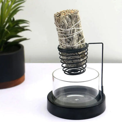 Nutshell black metal sage incense burner with glass base holding a smudge stick on white surface