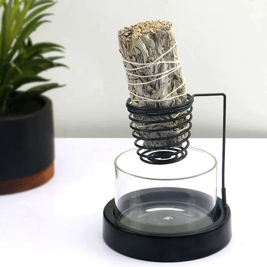 Nutshell black metal sage incense burner with glass base holding a smudge stick on white surface