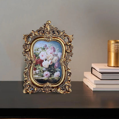 Vintage gold resin photo frame with ornate detailing showcasing floral artwork on a tabletop