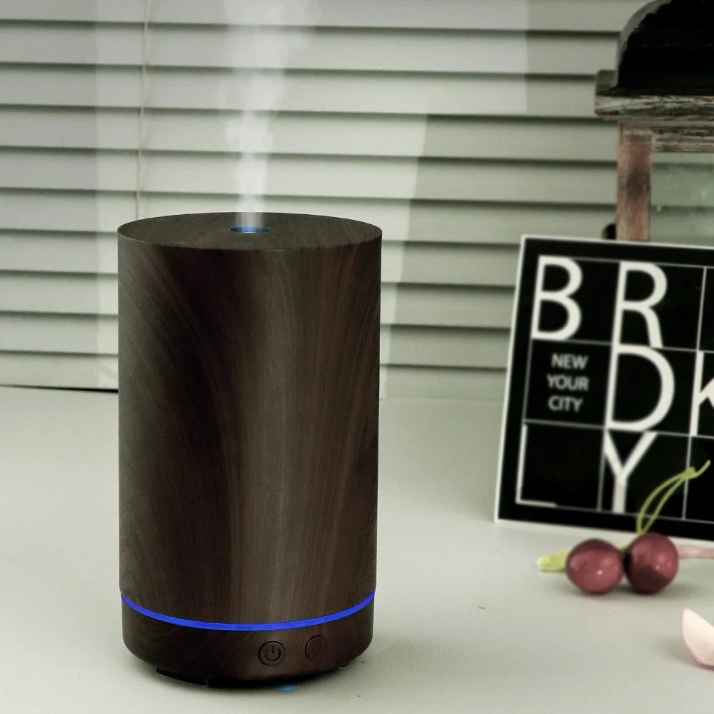 Nutshell wood grain essential oil diffuser emitting mist with blue LED light on white surface