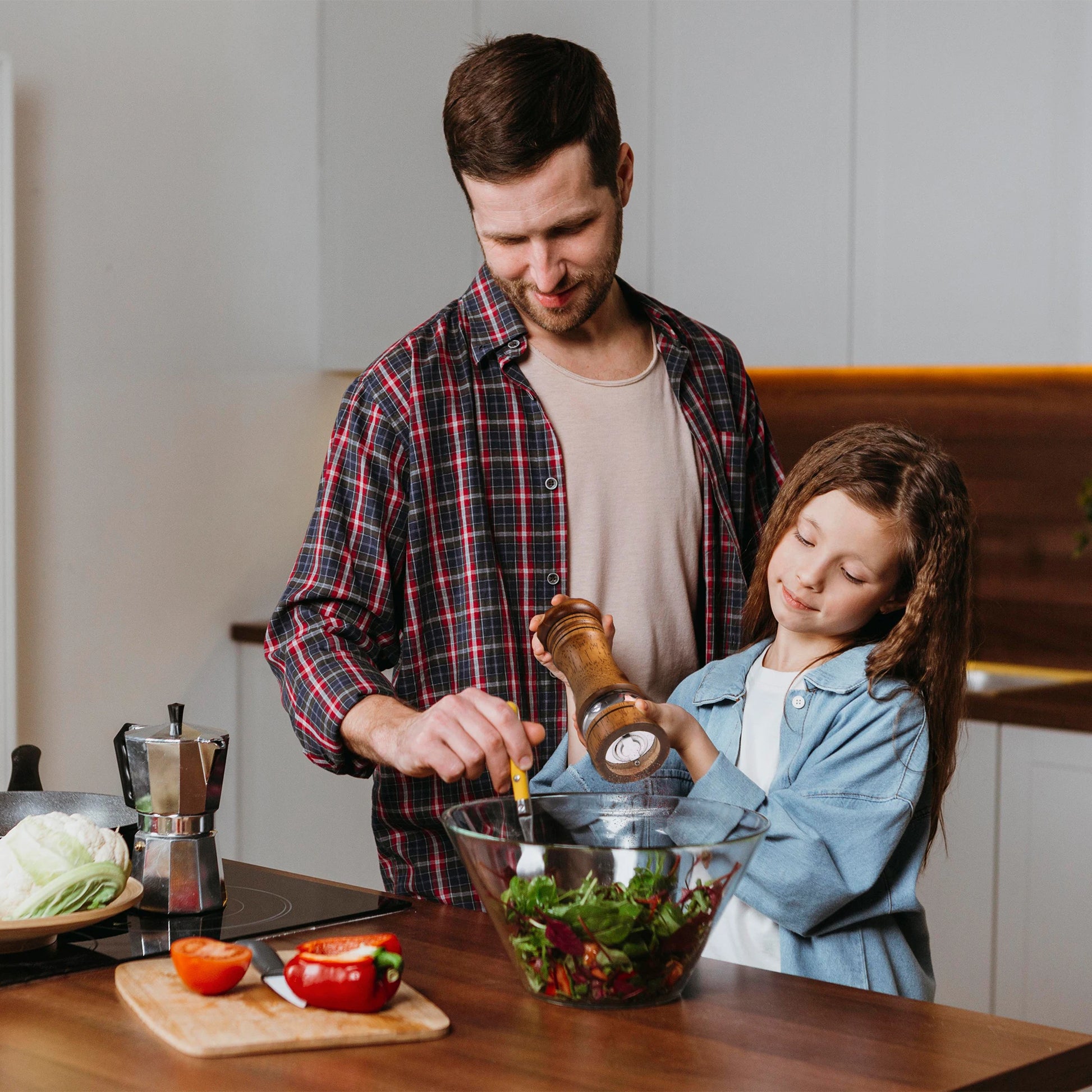 Father and daughter using wooden salt and pepper grinder set to season a fresh salad in kitchen