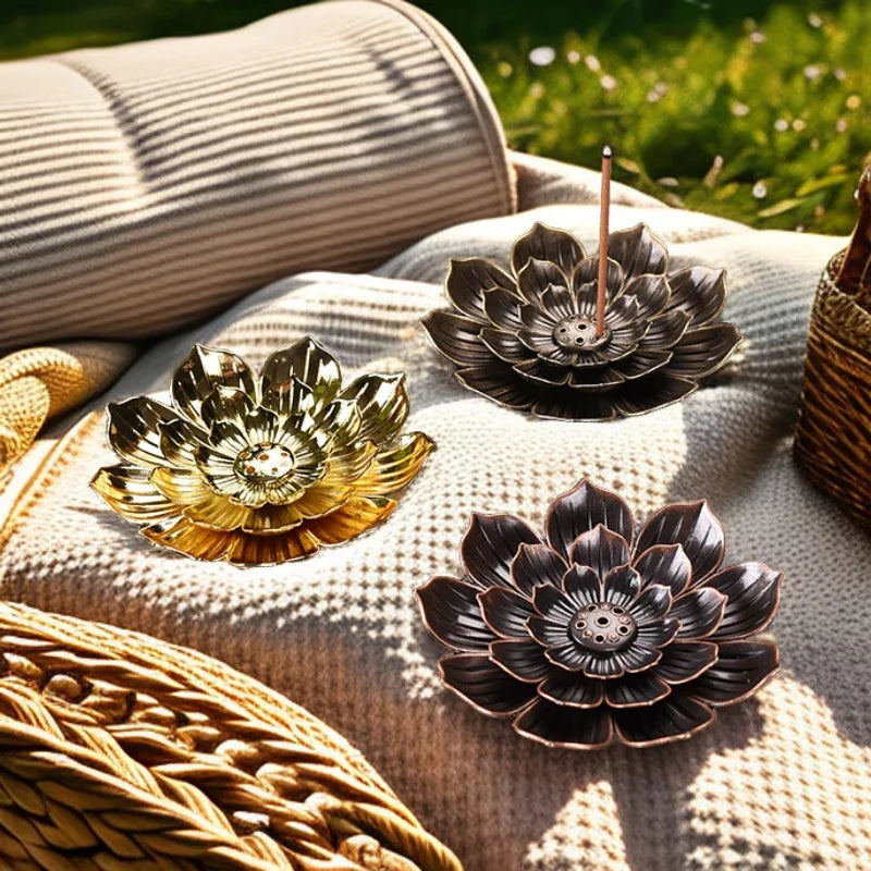 Nutshell Zen lotus incense burner trio in gold, bronze, and black metal on textured outdoor fabric