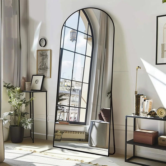 Nutshell arched full length floor mirror with black metal frame leaning in sunlit living room reflecting window view